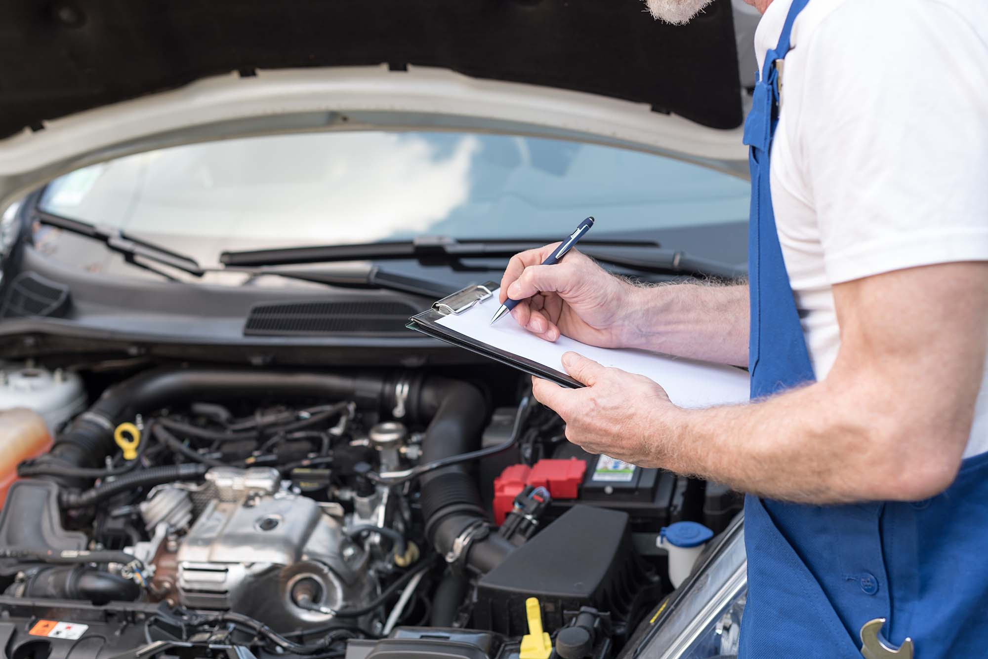 Car mechanic checking a car engine and writing on clipboard